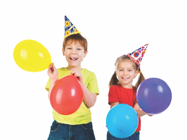 Two cheerful children wearing party hats and holding colorful balloons, laughing and celebrating.